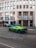 A vibrant green sports car is parked on a street in front of a building with large windows and signage that reads 'Credito Bergamasco'. The building has a modern architectural style with a series of vertical lines and is situated in an urban environment with tram tracks visible on the road. A few other cars are parked nearby, and pedestrians can be seen in the background.