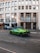 A vibrant green sports car is parked on a street in front of a building with large windows and signage that reads 'Credito Bergamasco'. The building has a modern architectural style with a series of vertical lines and is situated in an urban environment with tram tracks visible on the road. A few other cars are parked nearby, and pedestrians can be seen in the background.