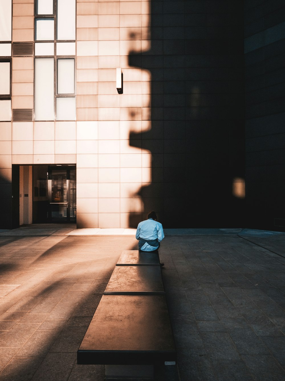 man in blue hoodie sitting on sidewalk during daytime