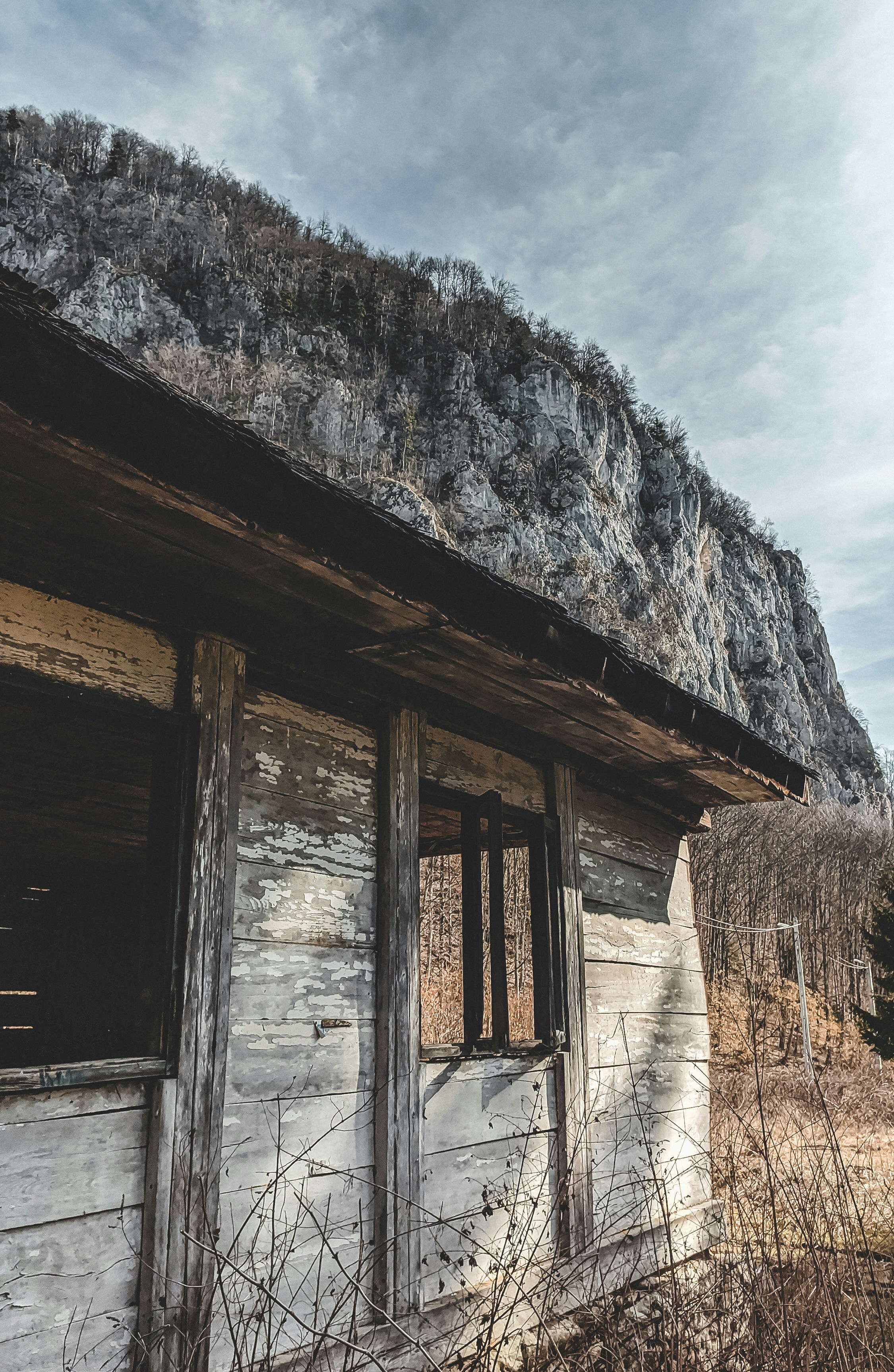 Casa de madera marrón cerca de la Montaña Rocosa Gris bajo un cielo nublado blanco durante el día