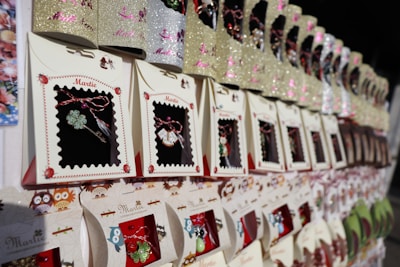 A display of neatly arranged decorative packs, each containing a small charm or trinket inside. The packaging features ornate designs with prominent floral or festive themes, and there are repetitive patterns of ladybugs and owls on the cards.