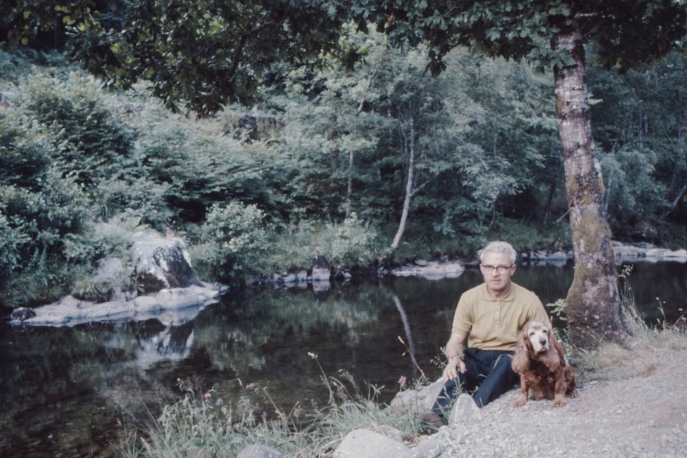 man in gray polo shirt sitting on rock near river during daytime