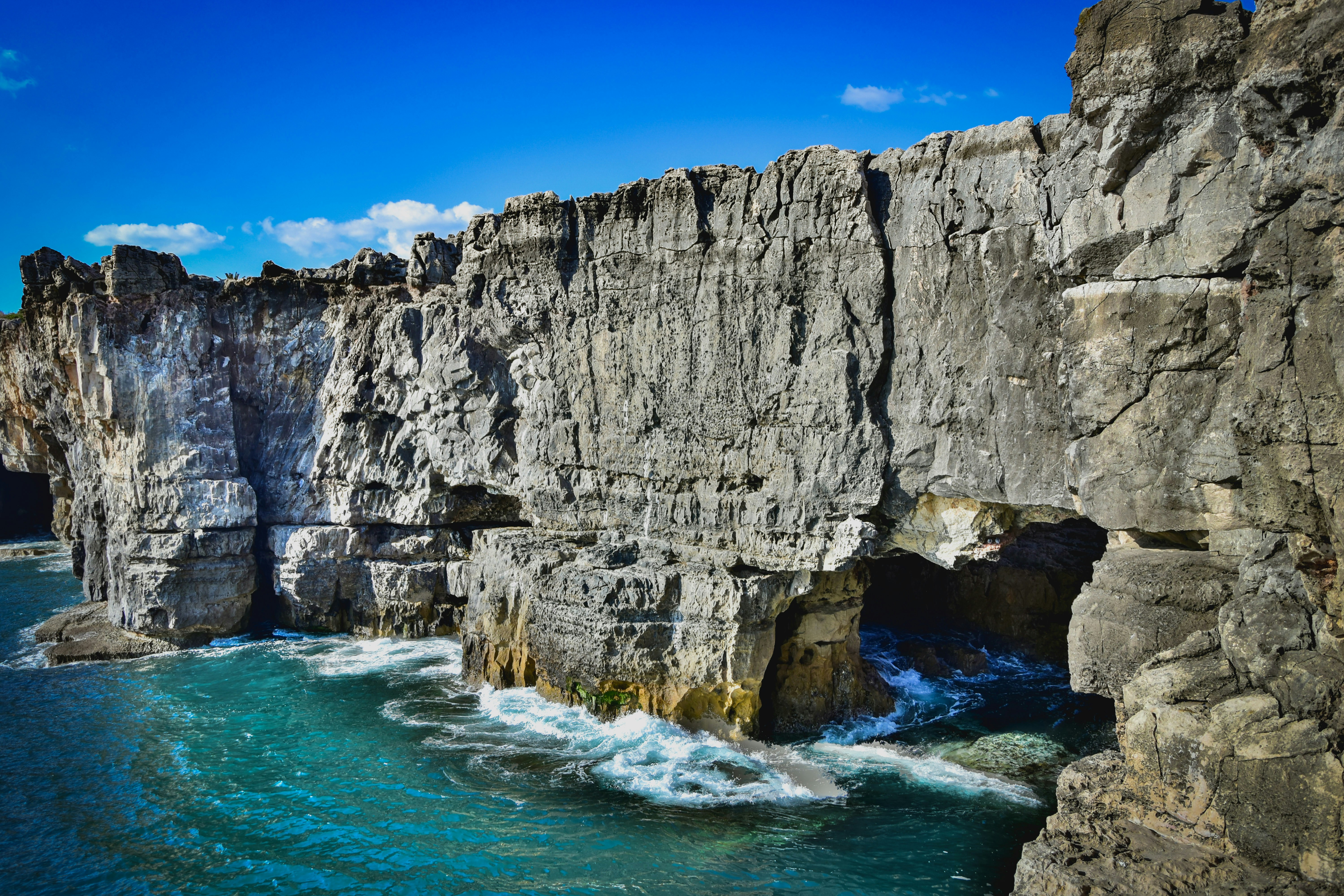 gray rocky mountain beside blue sea under blue sky during daytime