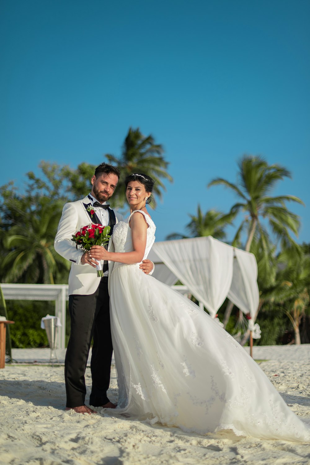 man in black suit and woman in white wedding dress standing on brown sand during daytime