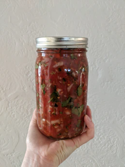 Close-up of a rustic jar filled with rich, red salsa macha surrounded by fresh chili peppers and garlic cloves