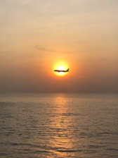 A sleek private jet soaring above a golden sunset over the ocean
