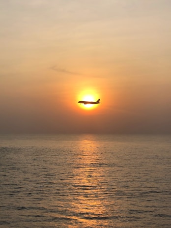 A sleek private jet soaring above a golden sunset over the ocean