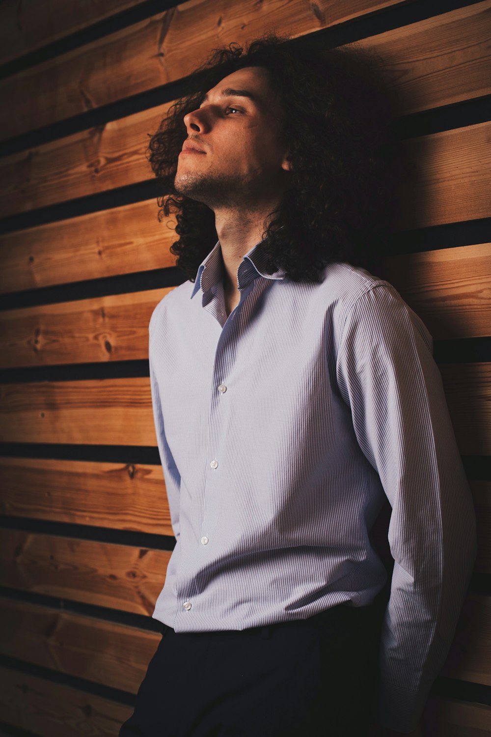 a man leaning against a wooden wall with his eyes closed