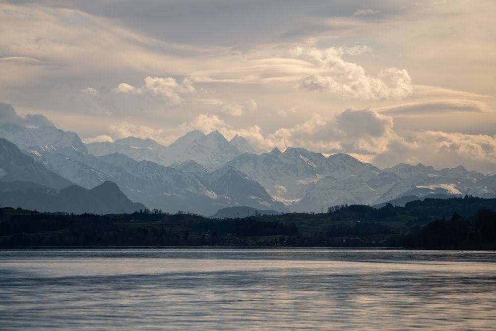 body of water near mountain under cloudy sky during daytime