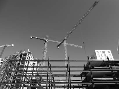 Cranes and construction sites dominate the view against a clear sky. The image captures several tower cranes and partially constructed buildings, with steel frameworks indicating ongoing development.