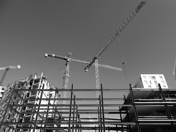 Cranes and construction sites dominate the view against a clear sky. The image captures several tower cranes and partially constructed buildings, with steel frameworks indicating ongoing development.
