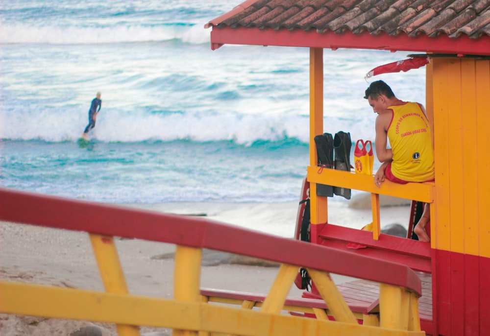 man in yellow shirt sitting on red wooden bench near sea during daytime