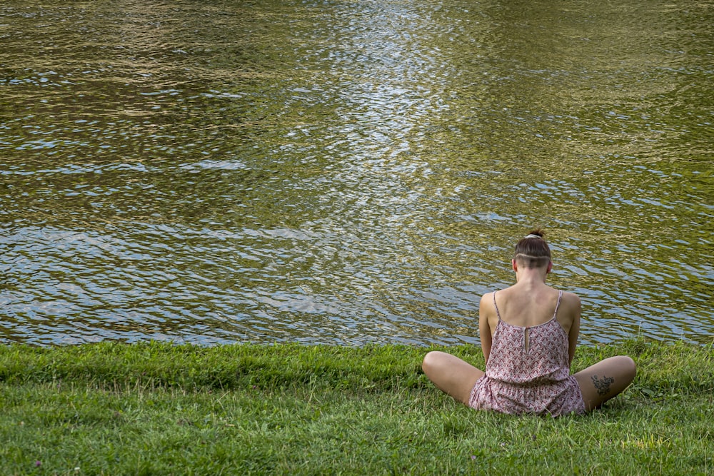 日中、水域近くの緑の芝生に座っている茶色のチューブドレスを着た女性