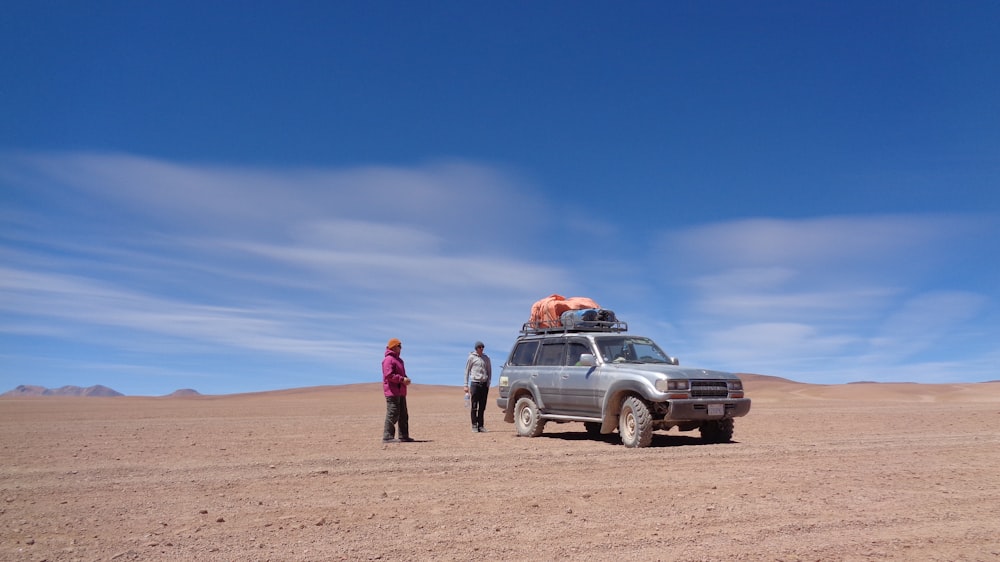 man and woman standing beside white suv on brown sand during daytime