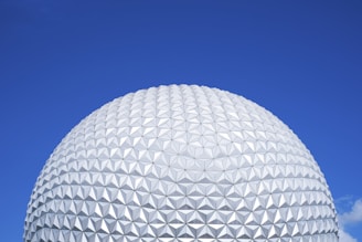 A large geodesic sphere with a geometric, patterned surface, set against a clear blue sky.