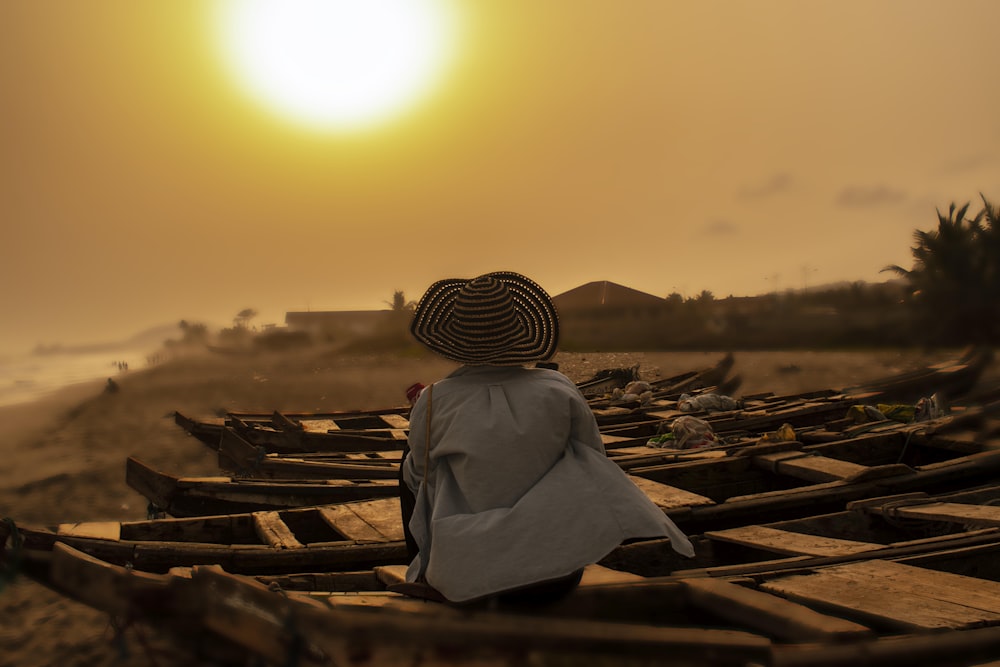 person in white robe and brown hat sitting on brown wooden bench during daytime