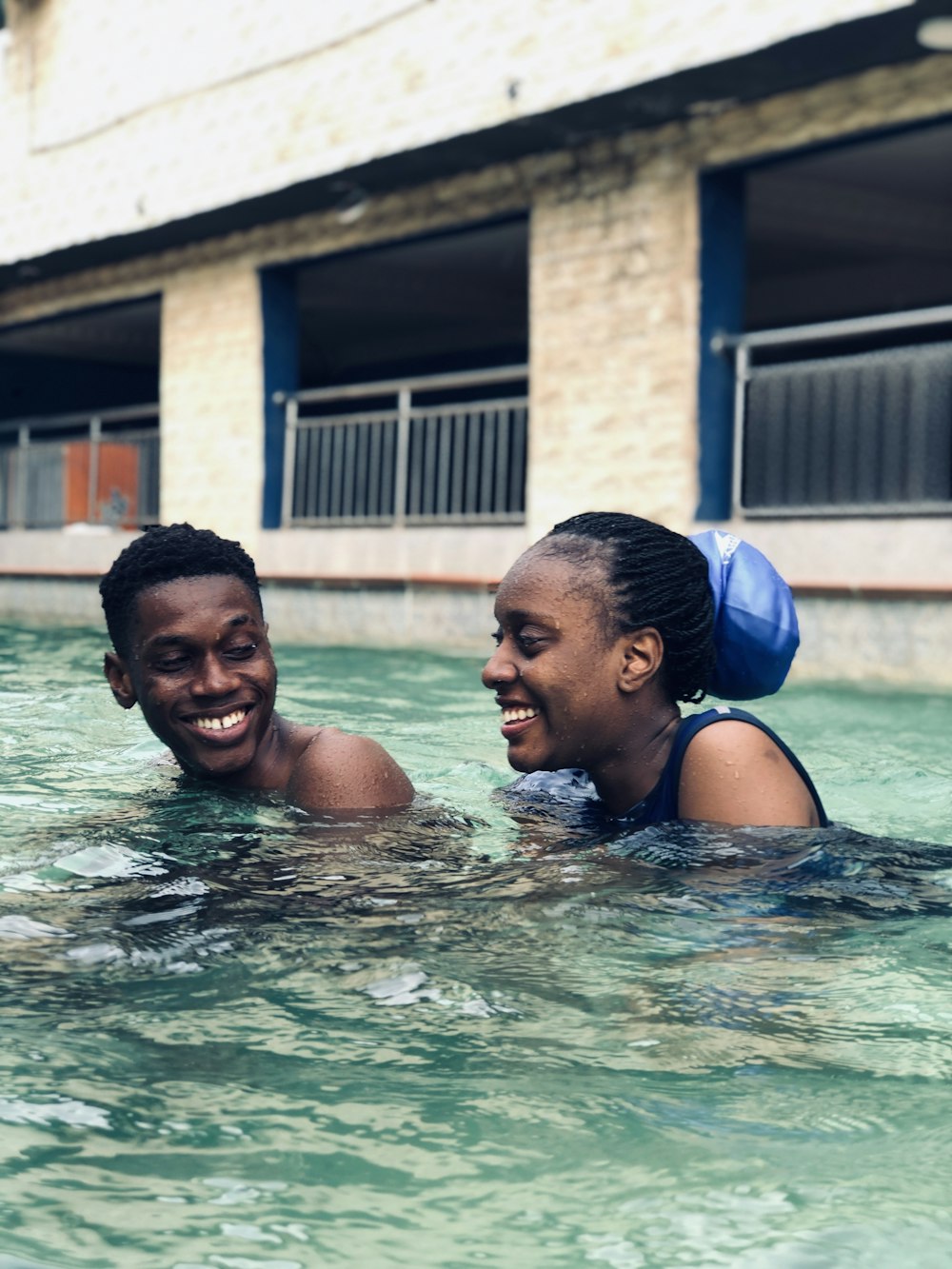 man in blue swimming cap kissing woman in blue bikini top in pool during daytime