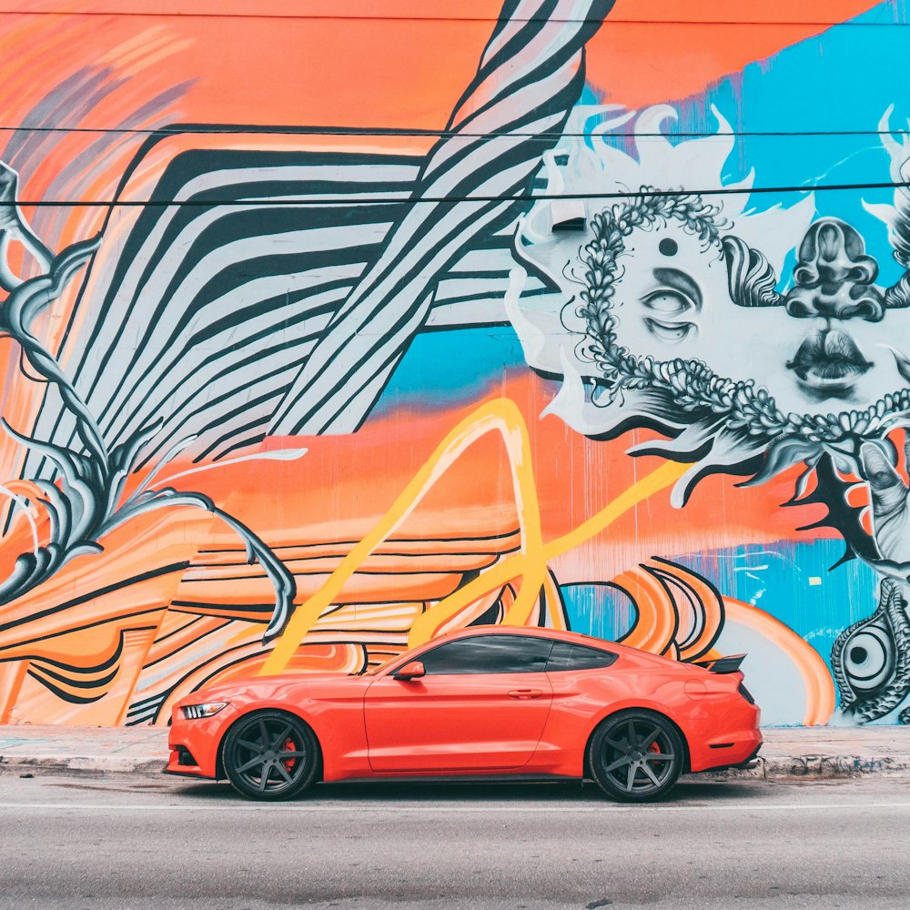 red car parked beside wall with graffiti