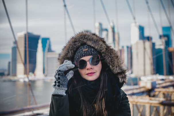 A close-up of a woman buttoning her fashionable hooded winter jacket in a city street setting.