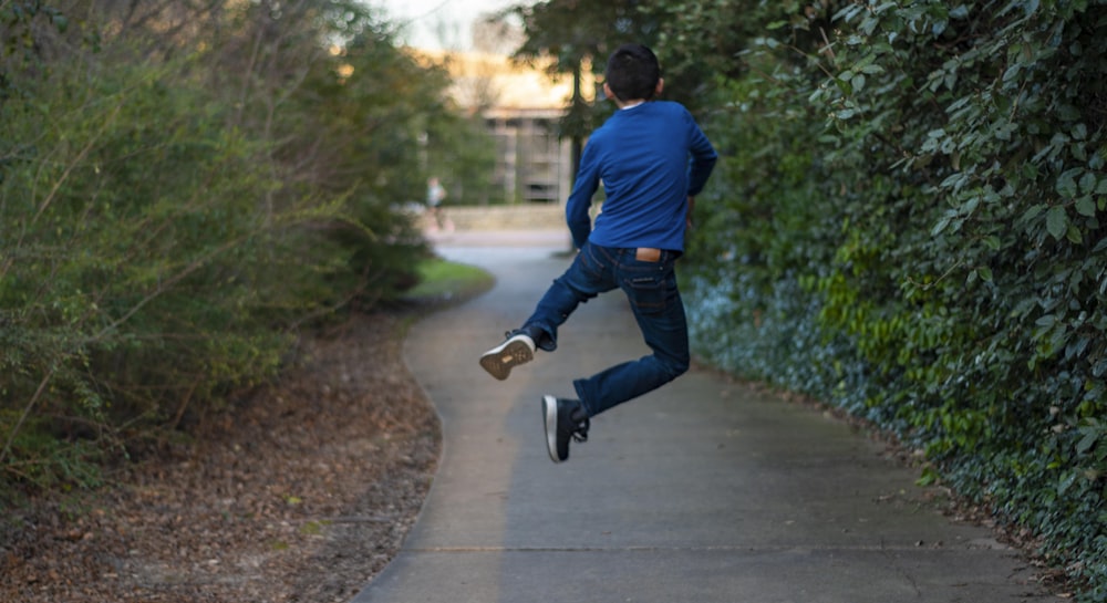 homme en chemise à manches longues bleue et jean en denim bleu marchant sur un sentier en béton gris pendant