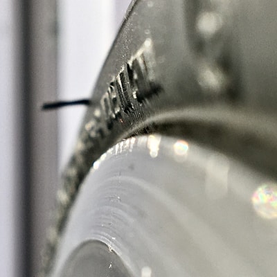 A close-up view of a metallic surface with a small protruding black pin or needle. The surface has embossed or engraved markings that seem to be text or numbers. The image captures the shiny and reflective texture of the metal.