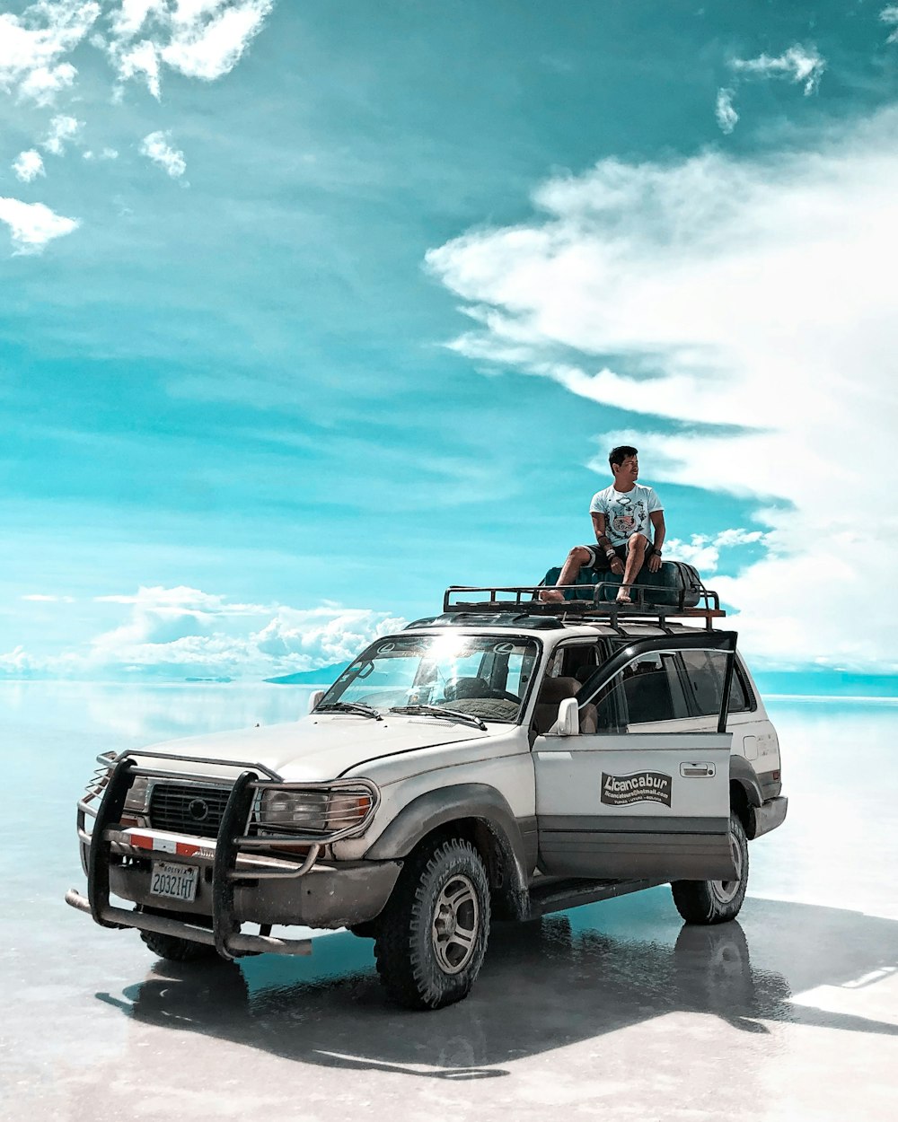 man in red jacket sitting on white suv on sea shore during daytime