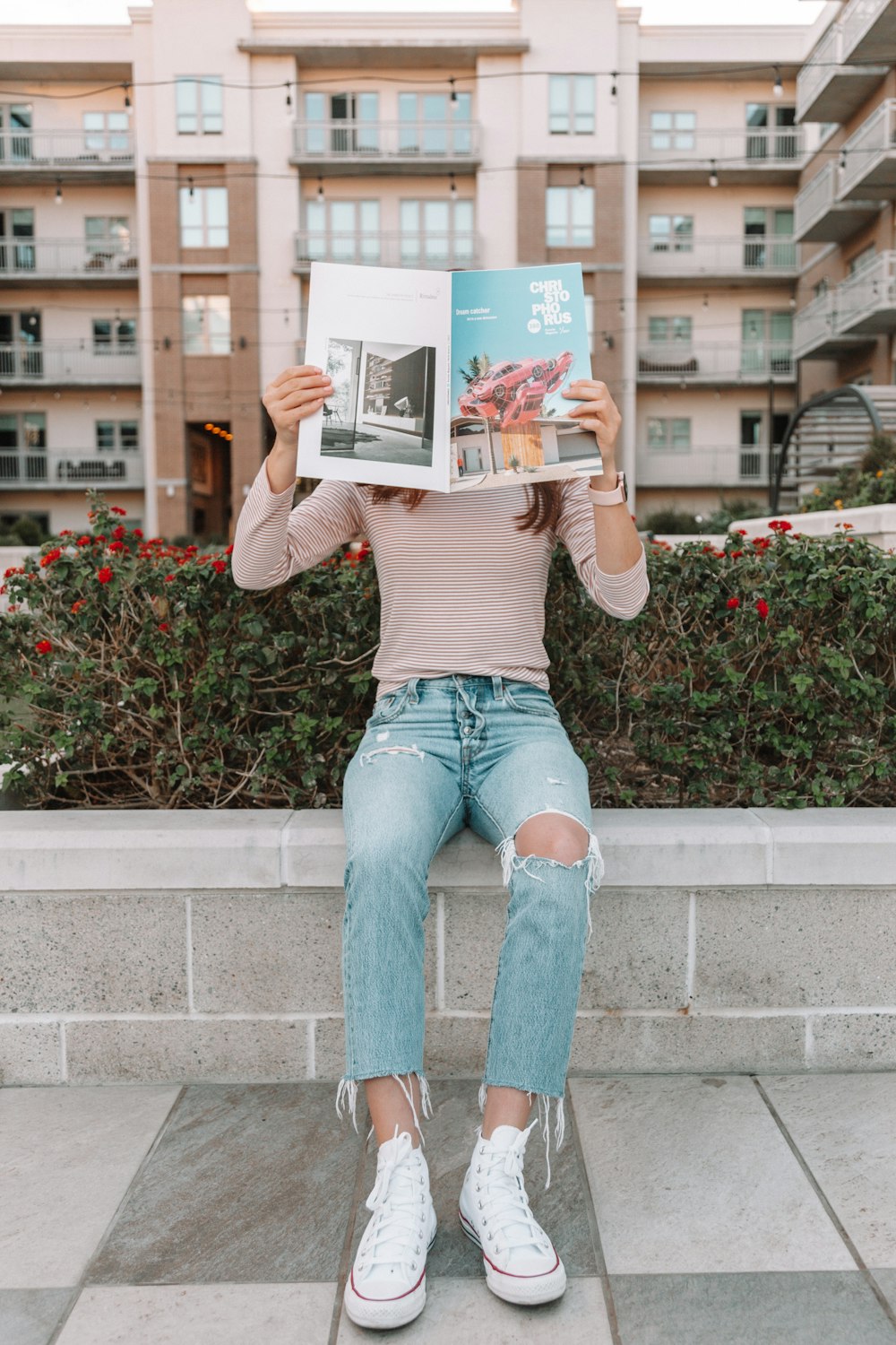 woman in brown long sleeve shirt and blue denim jeans sitting on concrete bench reading book