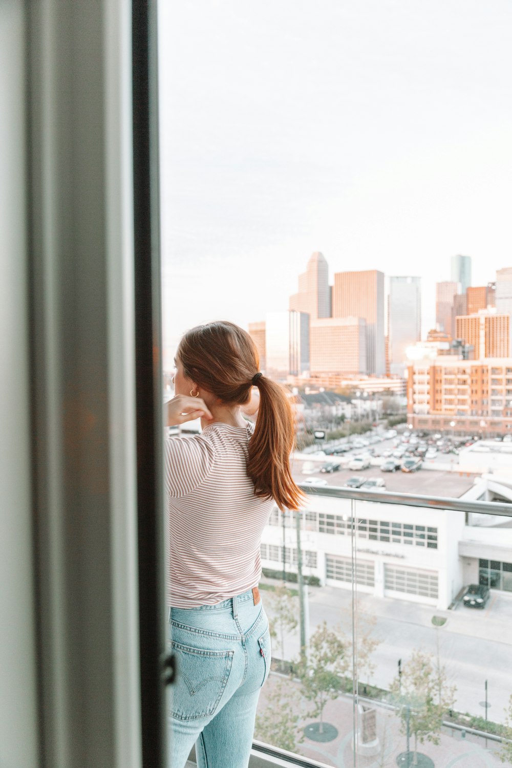 woman in white and black stripe shirt standing beside glass window during daytime