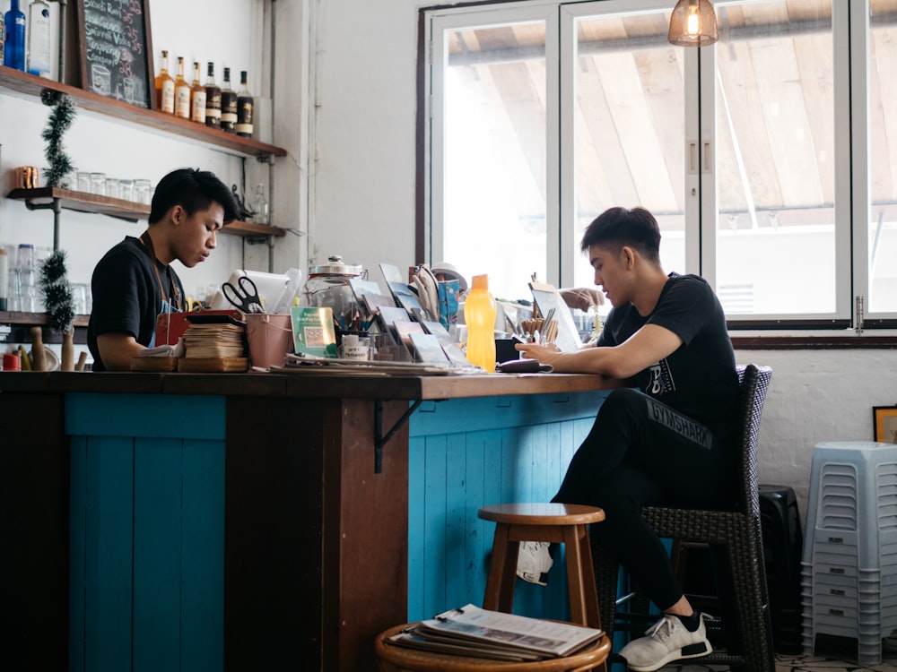 man in black crew neck t-shirt sitting on brown wooden chair