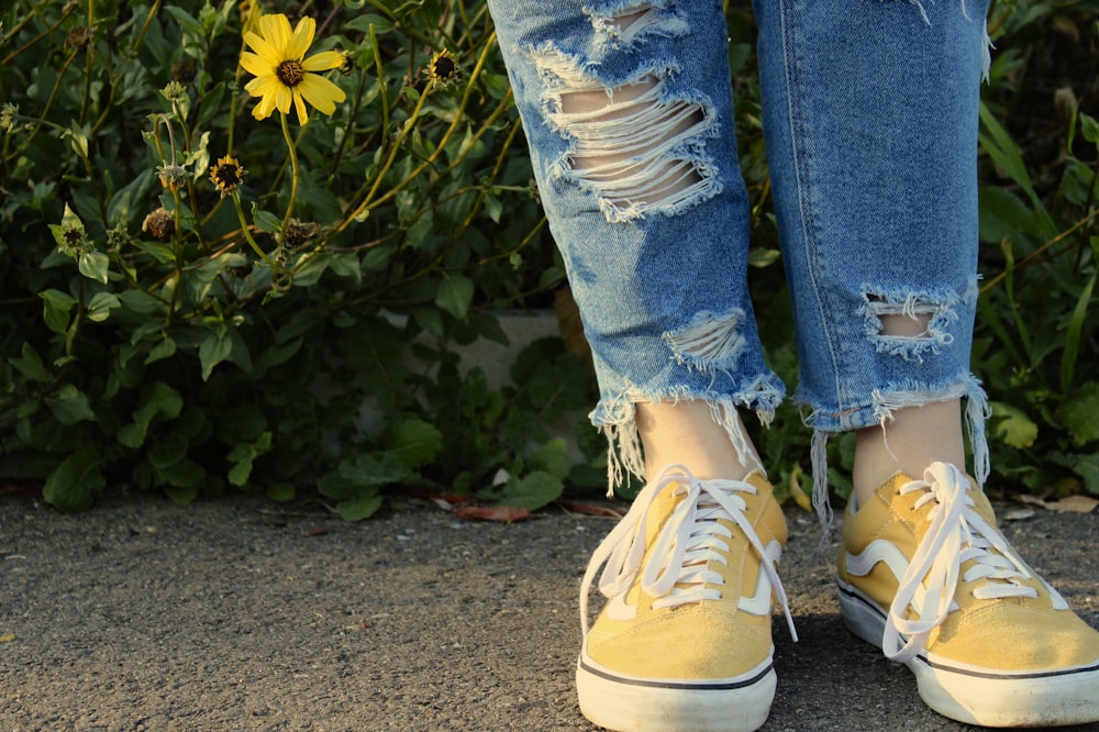 Persona con jeans de mezclilla azules y zapatillas blancas de pie sobre piso de concreto gris