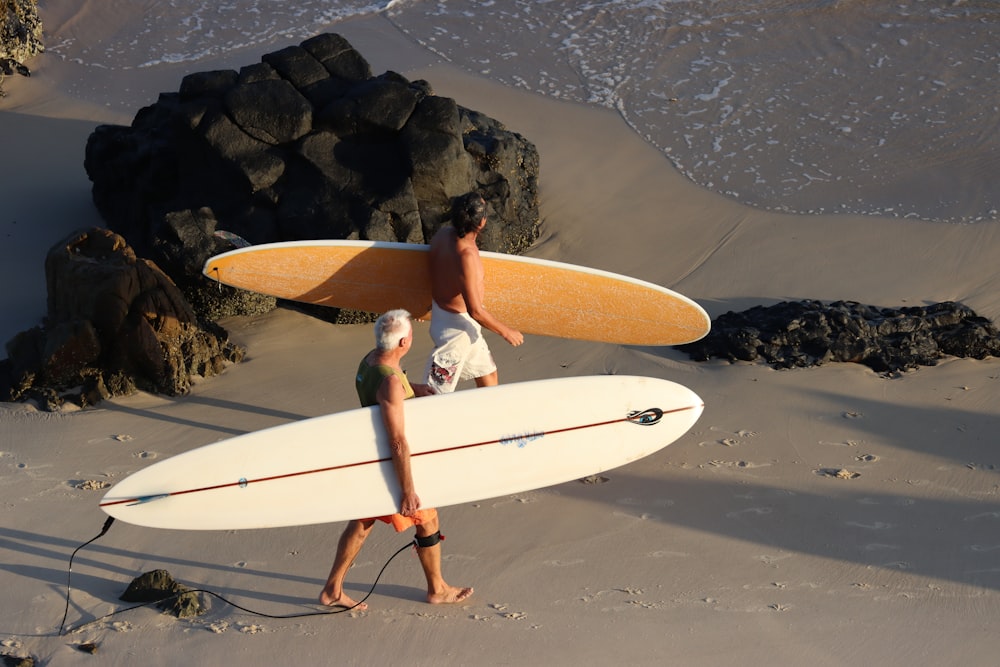 hombre en pantalones cortos azules sosteniendo una tabla de surf blanca en la playa durante el día