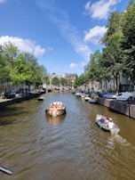 A canal lined with trees and historic buildings, bustling with boats carrying people enjoying a sunny day.