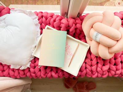 Cozy pastel pink-themed cushions and throws displayed on a rustic wooden bench