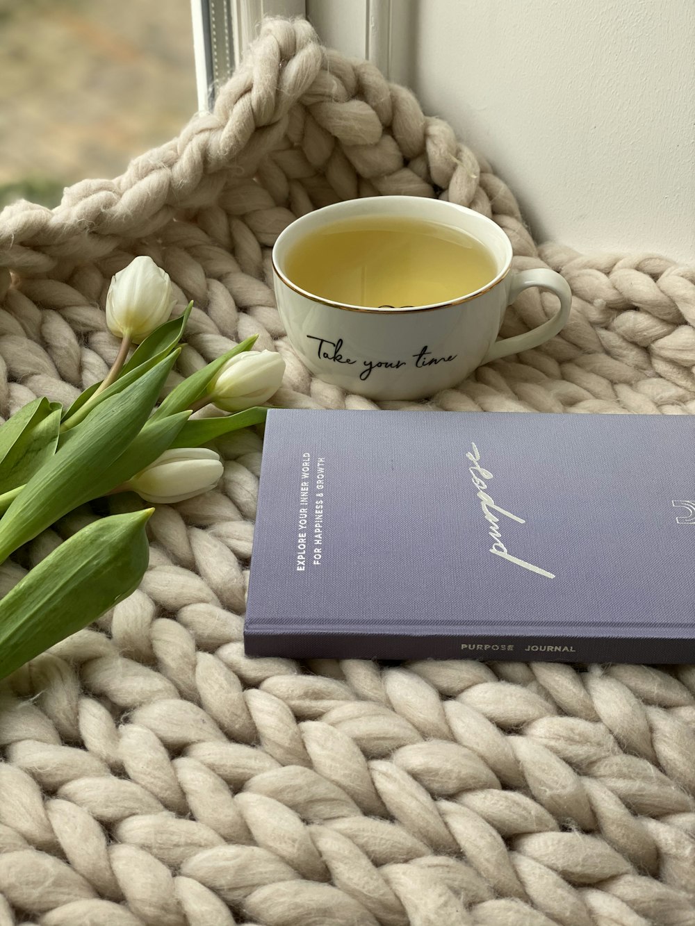 black book beside white ceramic mug on white knit textile