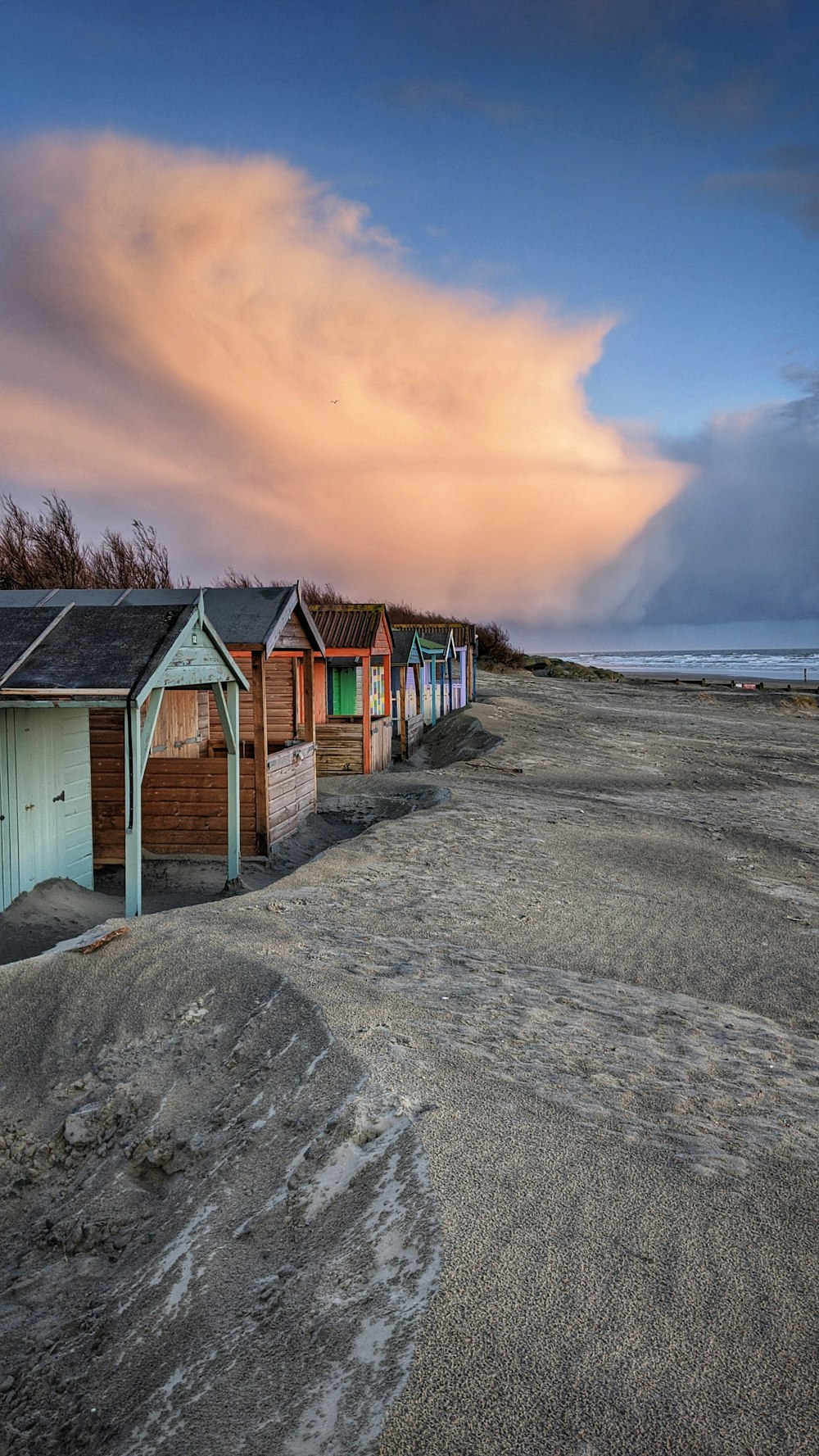 brown wooden houses on gray sand near body of water during sunset