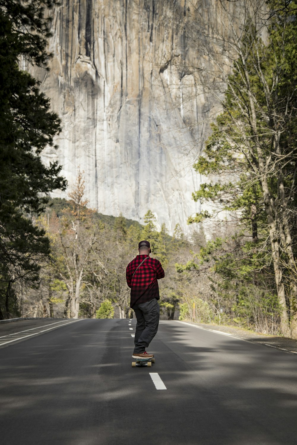 man in black and red plaid dress shirt and blue denim jeans standing on gray asphalt