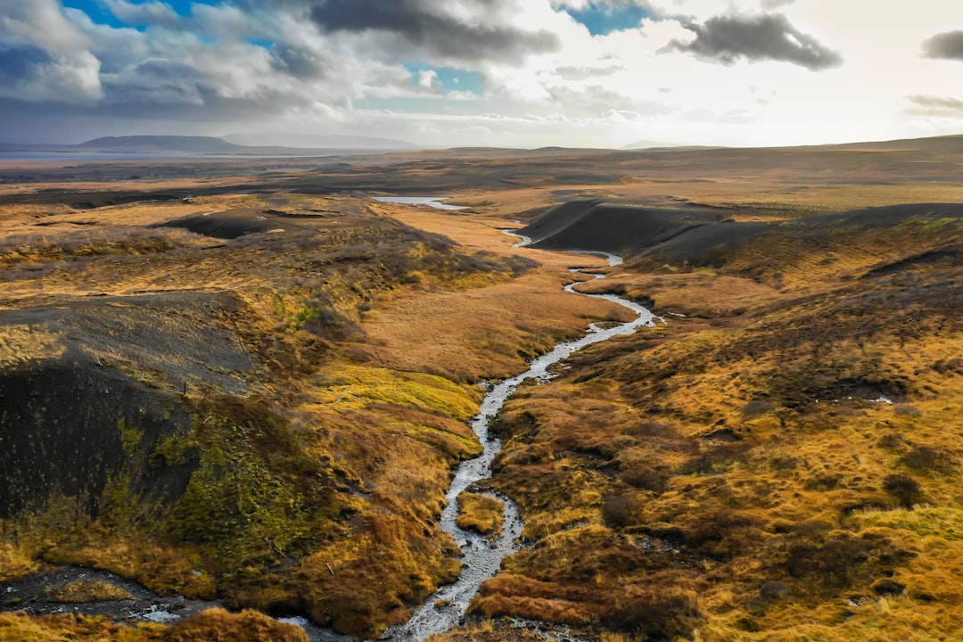 aerial view of river between brown field under cloudy sky during daytime