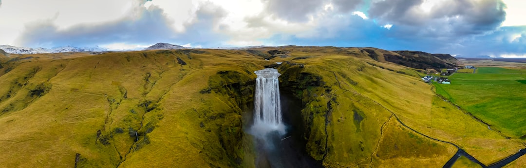 waterfalls on brown and green mountain under white clouds during daytime