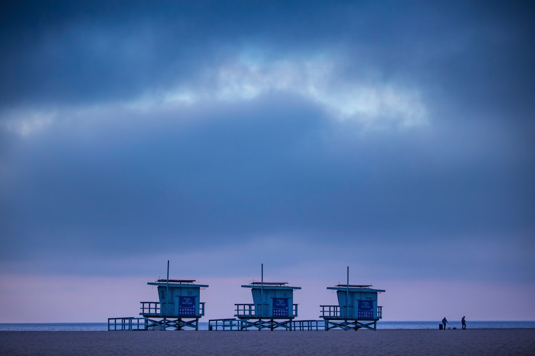 white and blue wooden house on beach under gray clouds