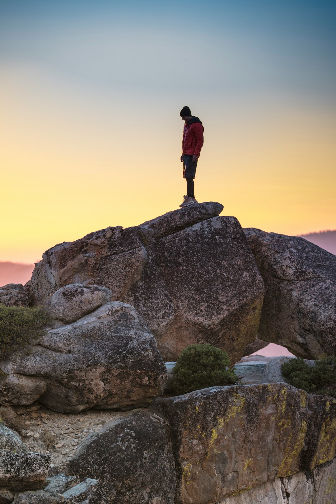 man in black jacket standing on rock formation during sunset