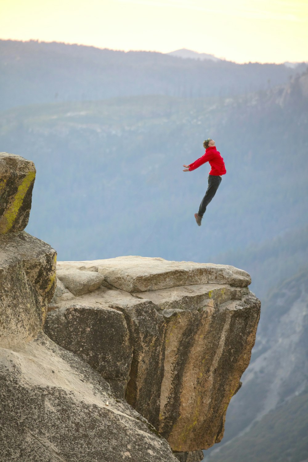 man in red long sleeve shirt and black pants jumping on brown rock during daytime