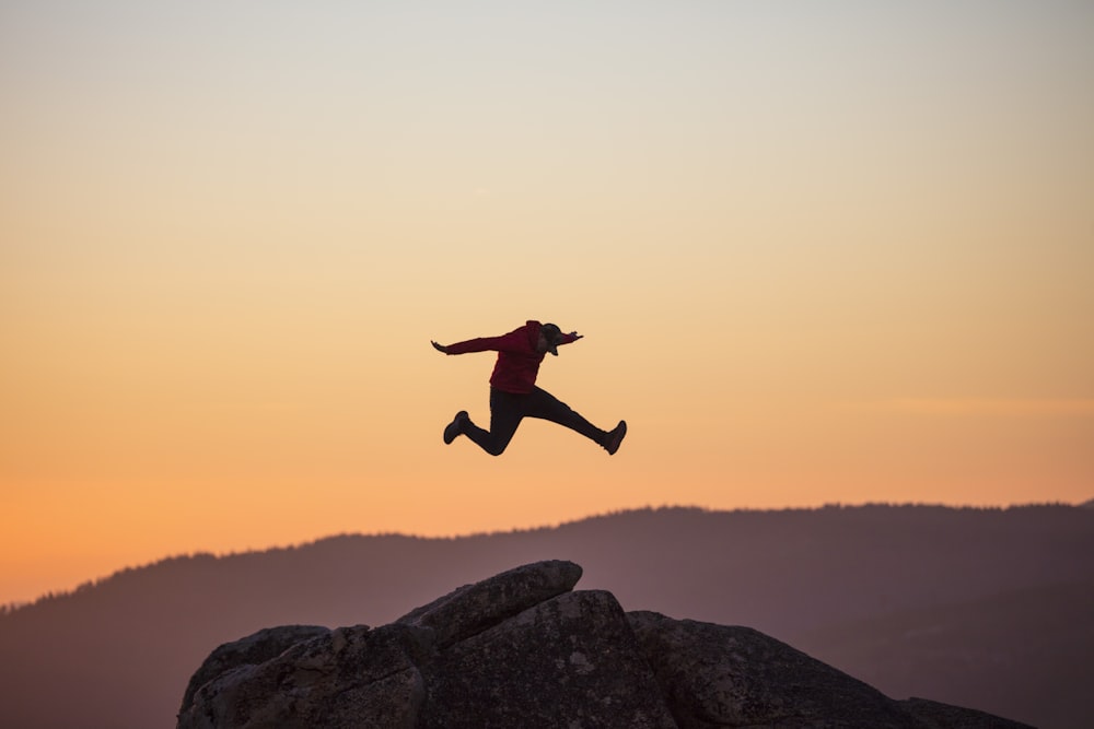 man jumping on rocky mountain during daytime