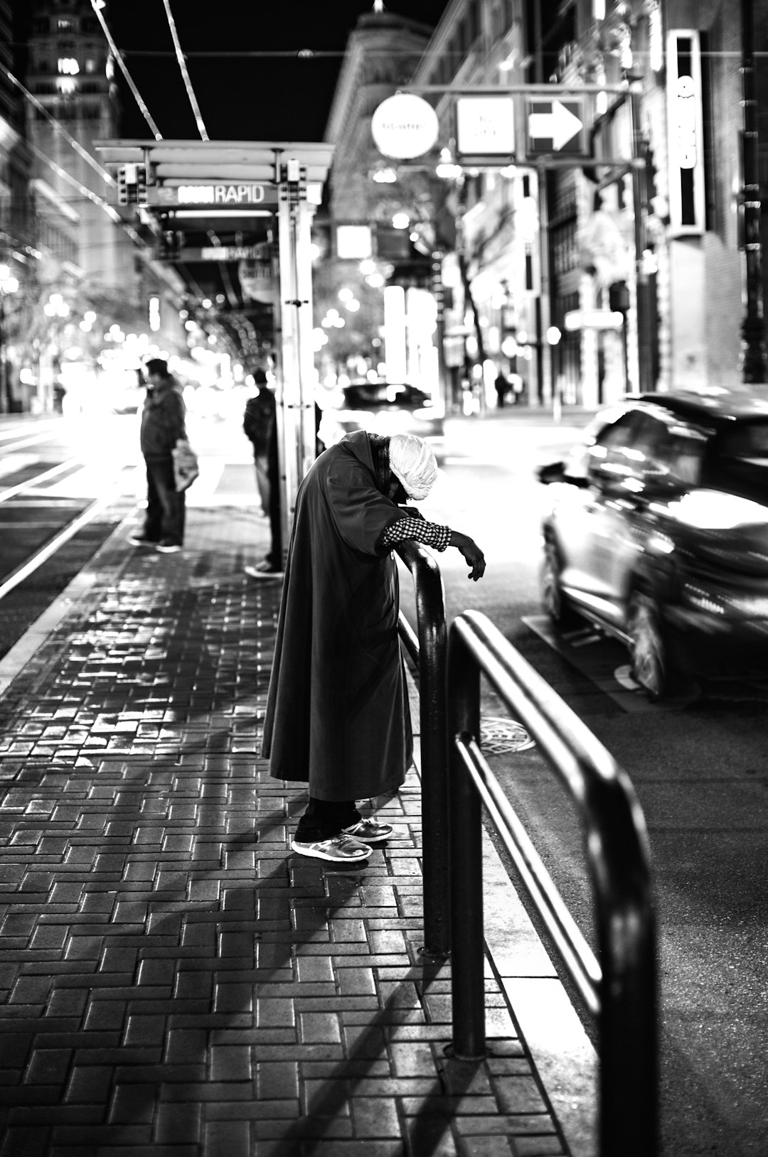 grayscale photo of woman in coat standing on sidewalk