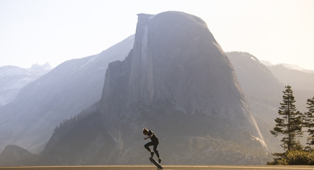 man in black jacket and pants jumping on brown rock mountain during daytime
