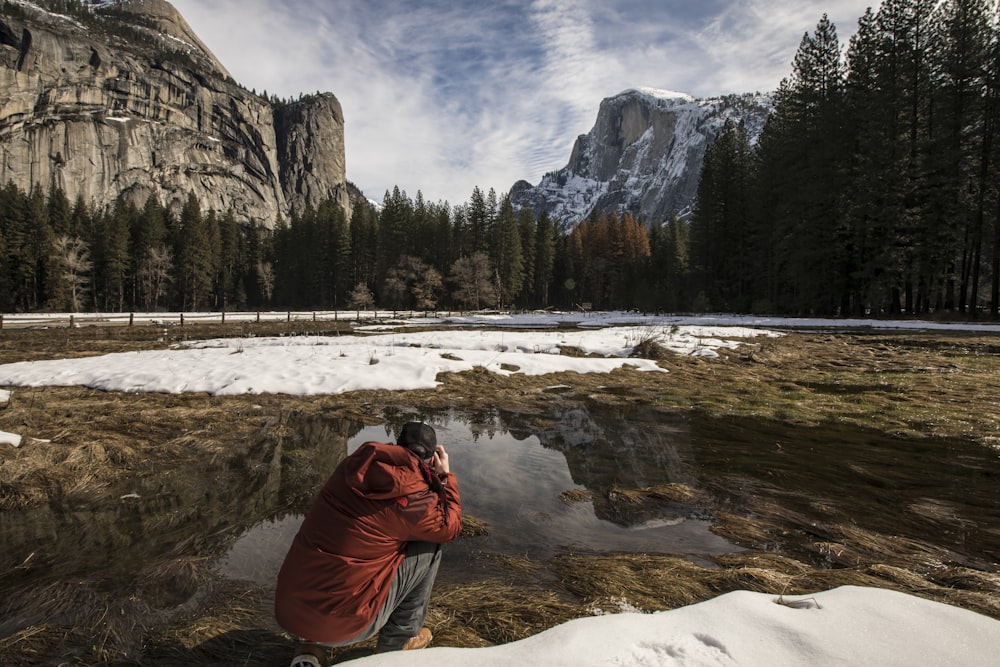 man in red hoodie taking photo of lake