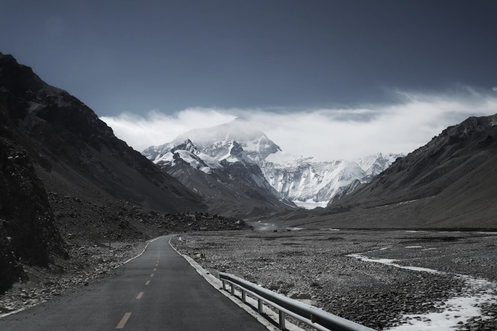 gray concrete road near snow covered mountains under blue sky during daytime