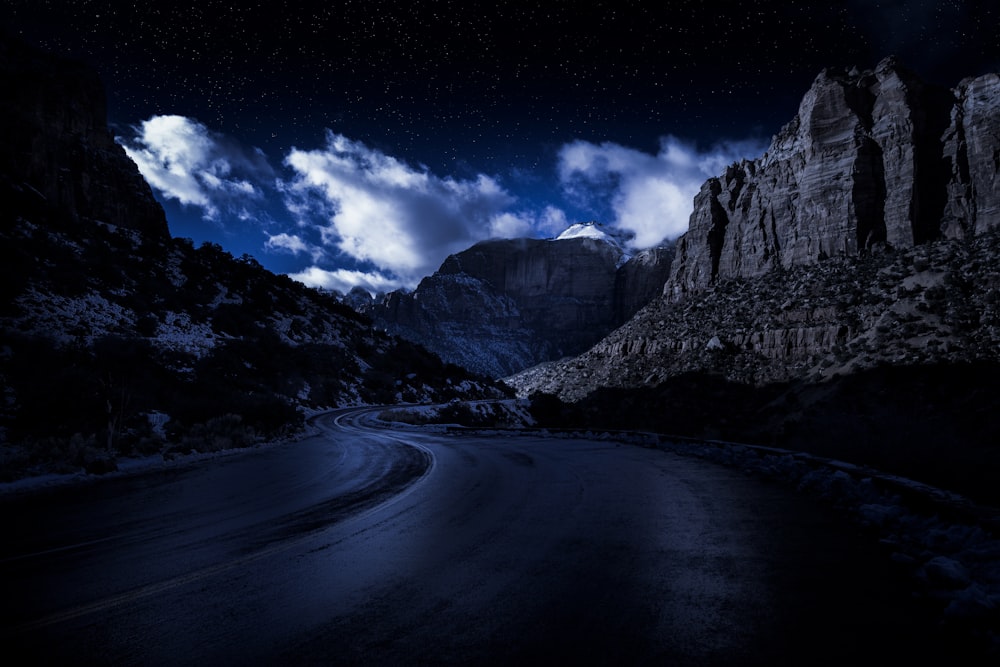 gray road between gray rocky mountains under blue sky during daytime