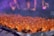 Skewers of marinated meat roasting over a grill with a smoky atmosphere. The background features blurred, colorful lights creating a festive ambiance.