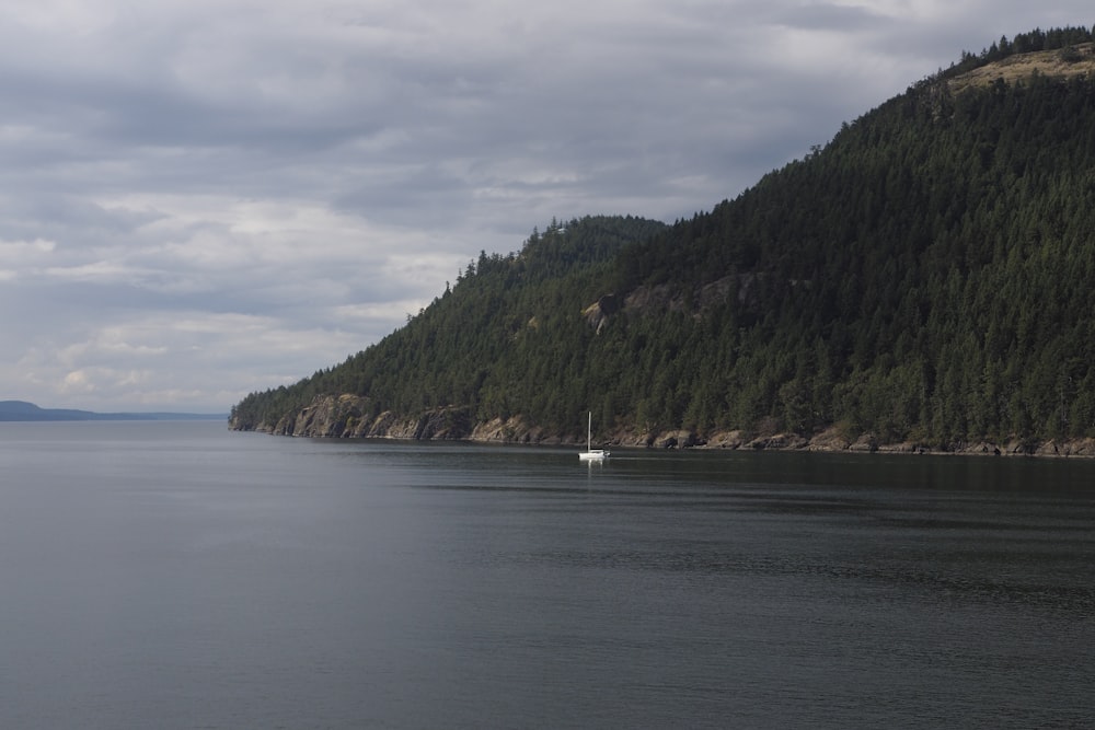 white boat on sea near green mountain under white clouds during daytime