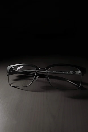Close-up of sleek black optical frames resting on a white surface with soft shadows.